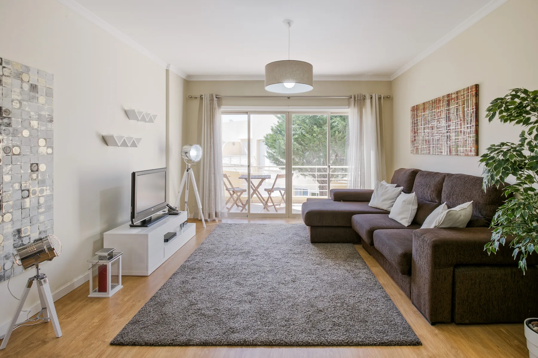 A bright living room with a sectional sofa facing a television and glass doors to a balcony.