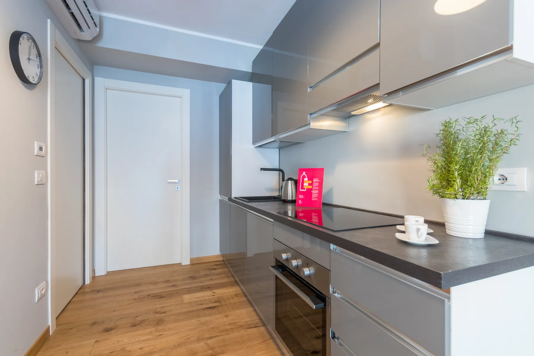 Una cocina moderna con gabinetes grises, una encimera oscura y suelo de madera.