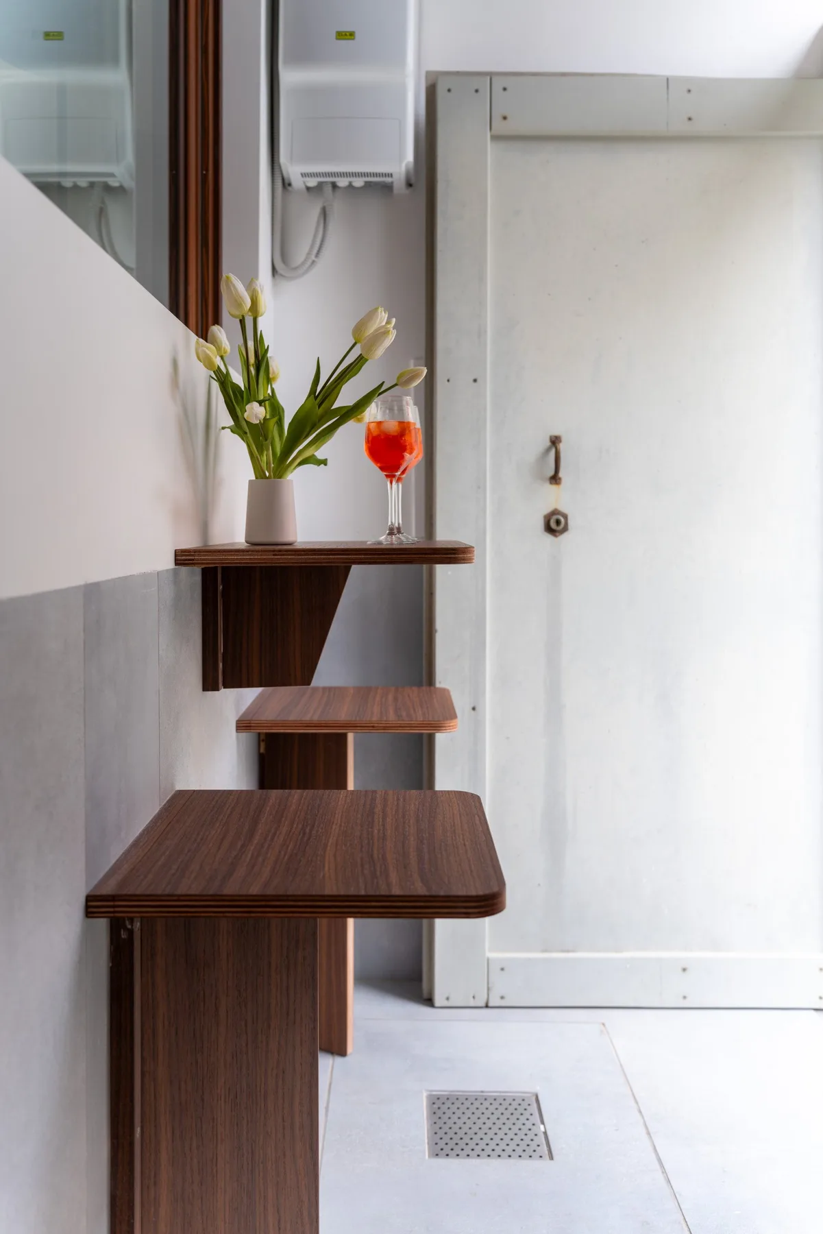 Un baño compacto cuenta con un mueble de madera oscura, flores y una copa con una bebida roja.