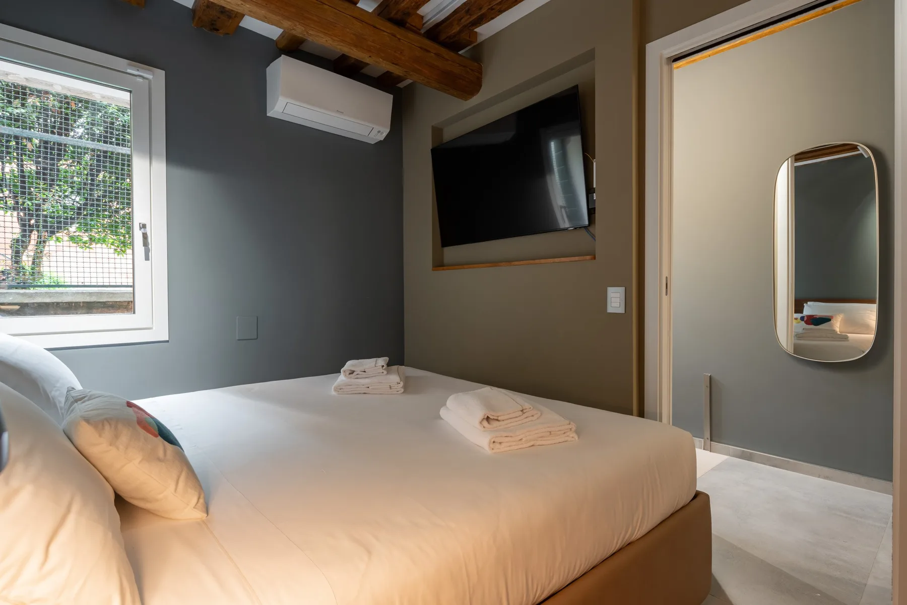 Un dormitorio con una cama bien tendida y una ventana con vista a la vegetación.