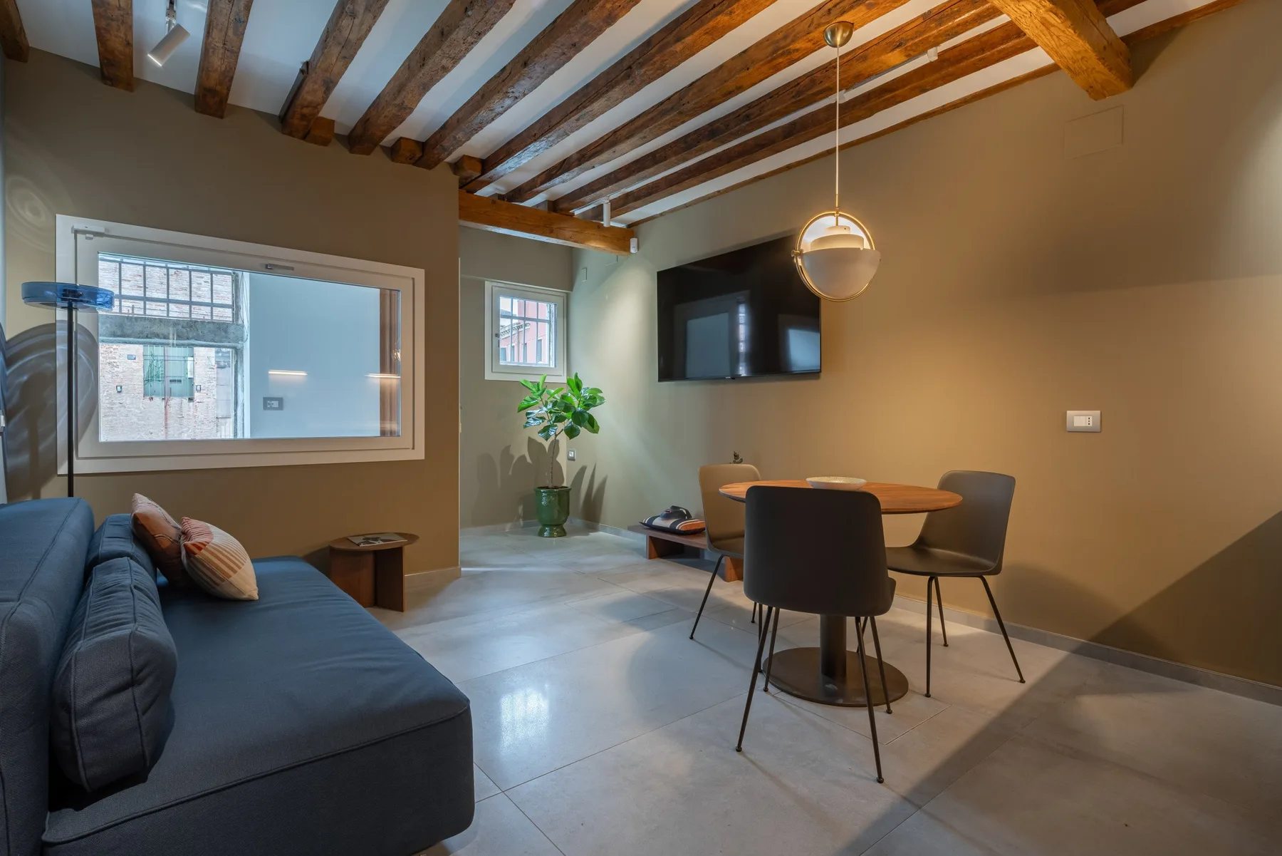 Una sala de estar y comedor con sofá oscuro, mesa y televisor en la pared.