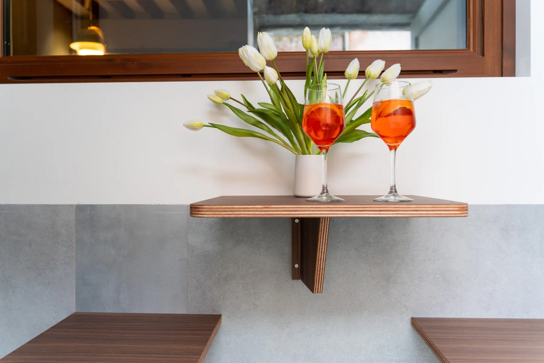 Un pequeño estante de pared muestra dos bebidas anaranjadas junto a flores blancas.