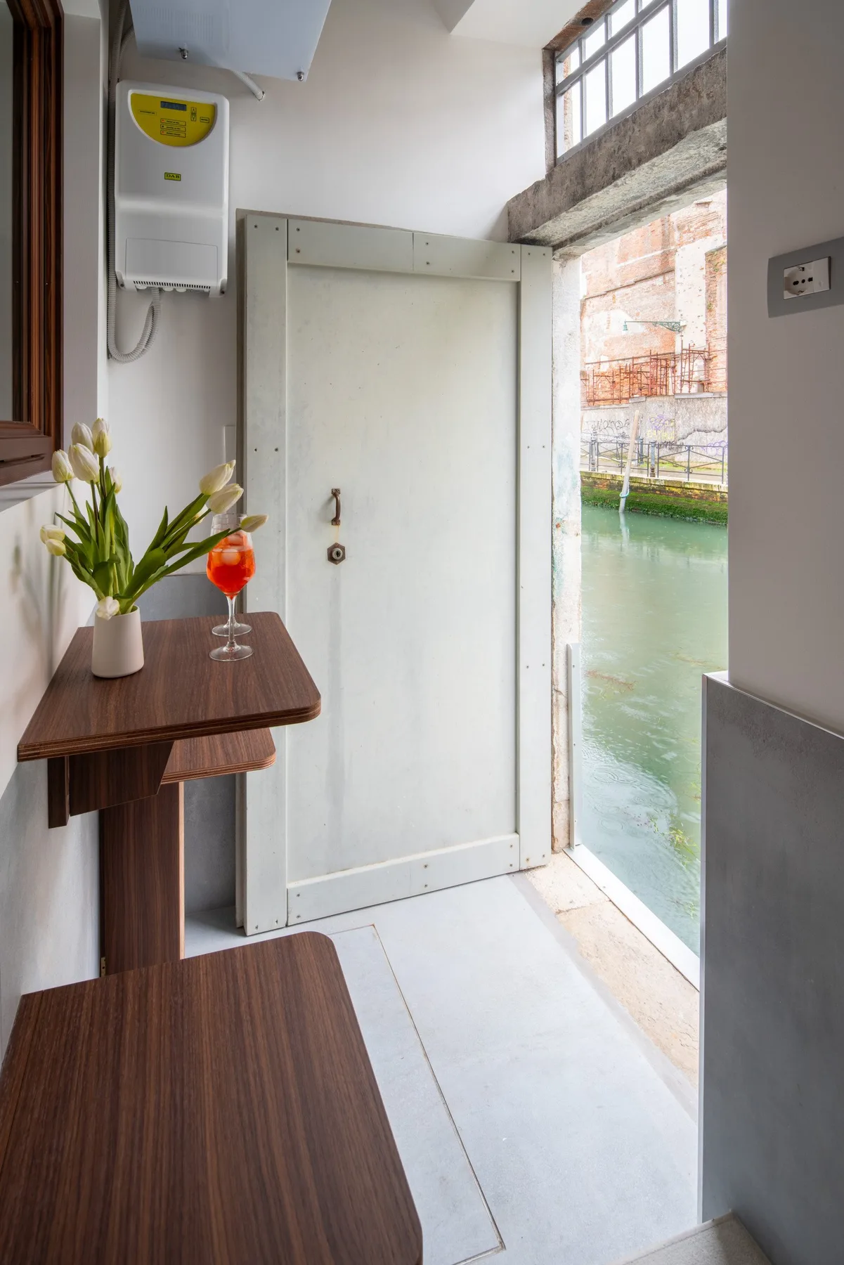 Una entrada interior estrecha da a un canal, con una mesa pequeña junto a la puerta.