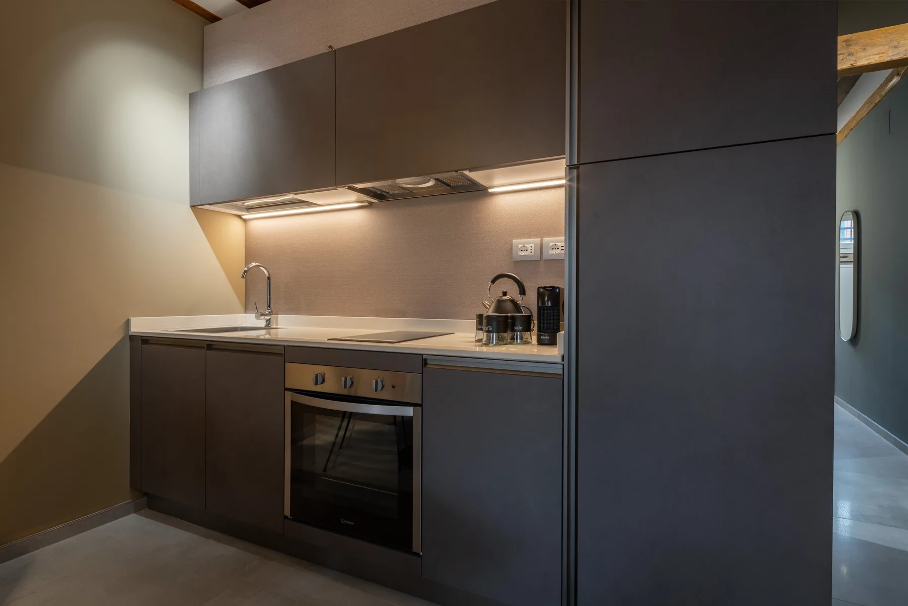 Una cocina compacta con gabinetes oscuros, un horno empotrado y electrodomésticos sobre la encimera.