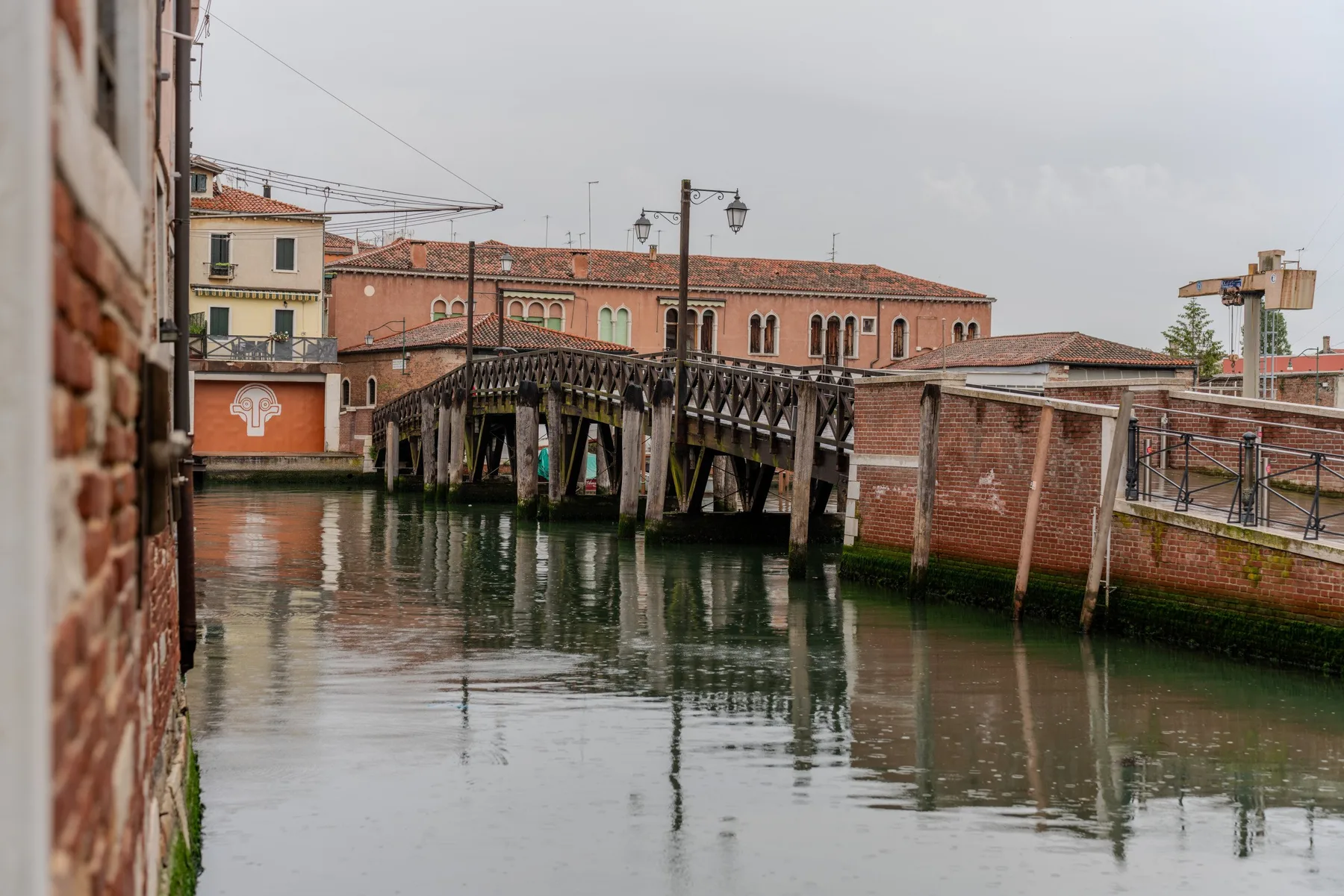 Un puente de madera cruza un canal junto a edificios de ladrillo.