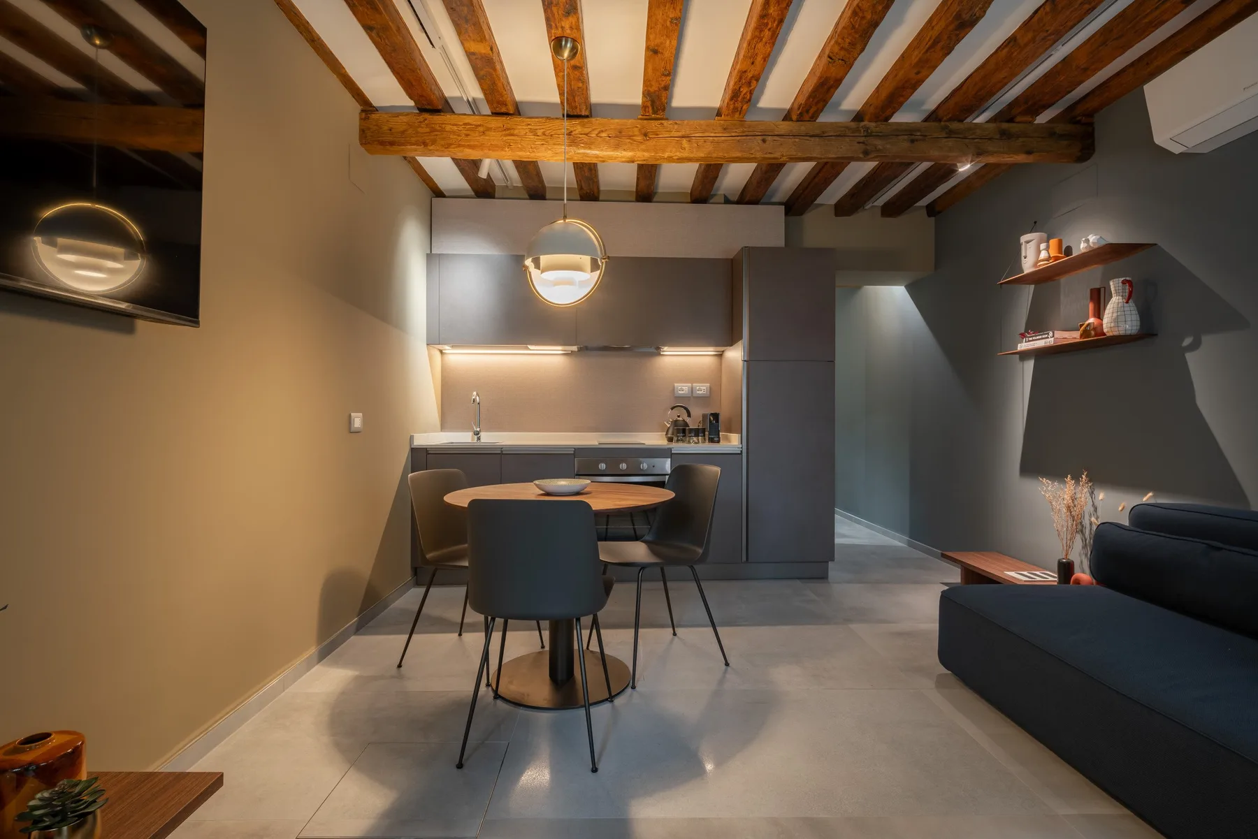A modern open-plan living and dining area with a compact kitchen and exposed ceiling beams.