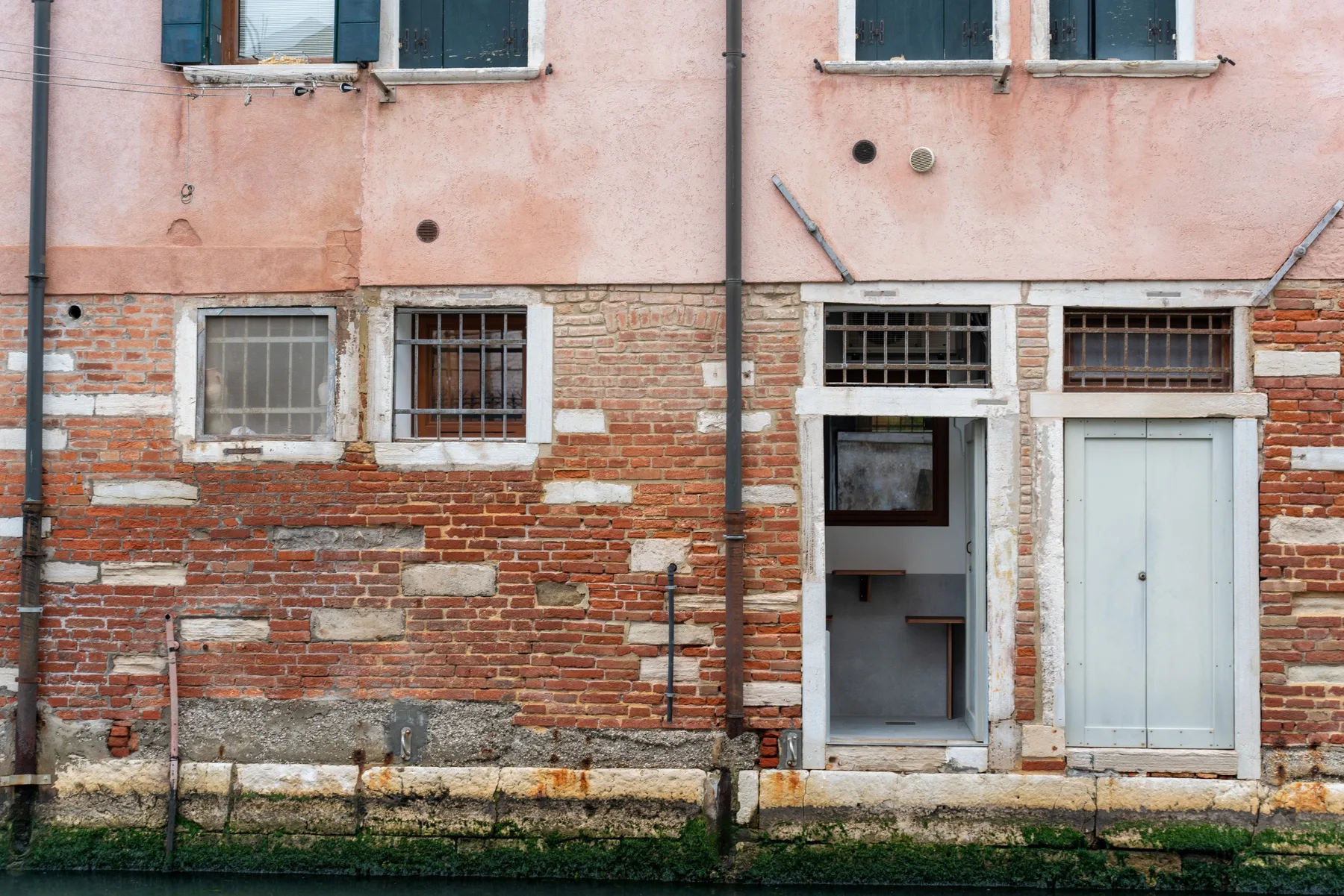Una fachada desgastada con ladrillo, ventanas y puertas junto a un canal.
