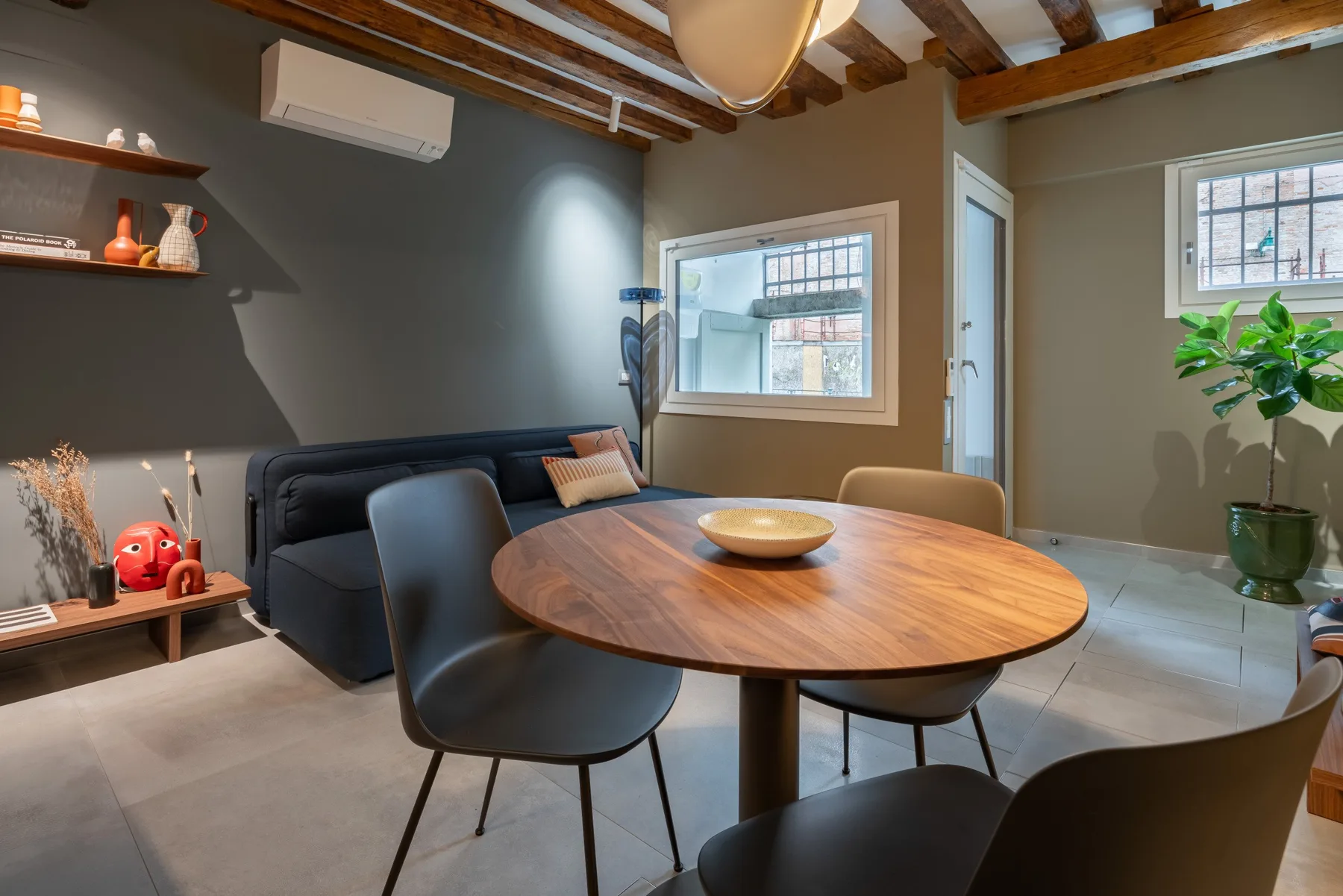 Un comedor con una mesa redonda de madera, asientos y una ventana grande.
