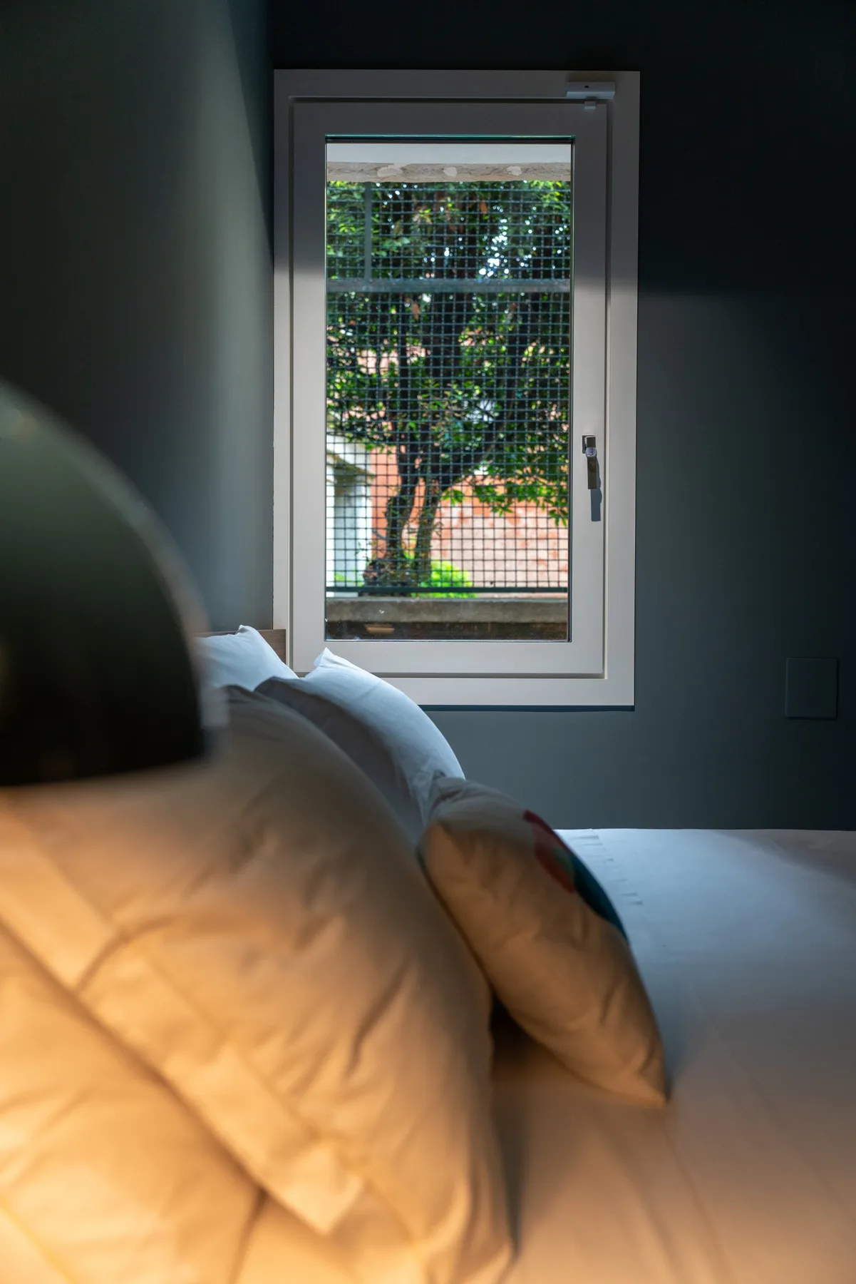 Un dormitorio con una cama junto a una ventana que da a una arboleda.