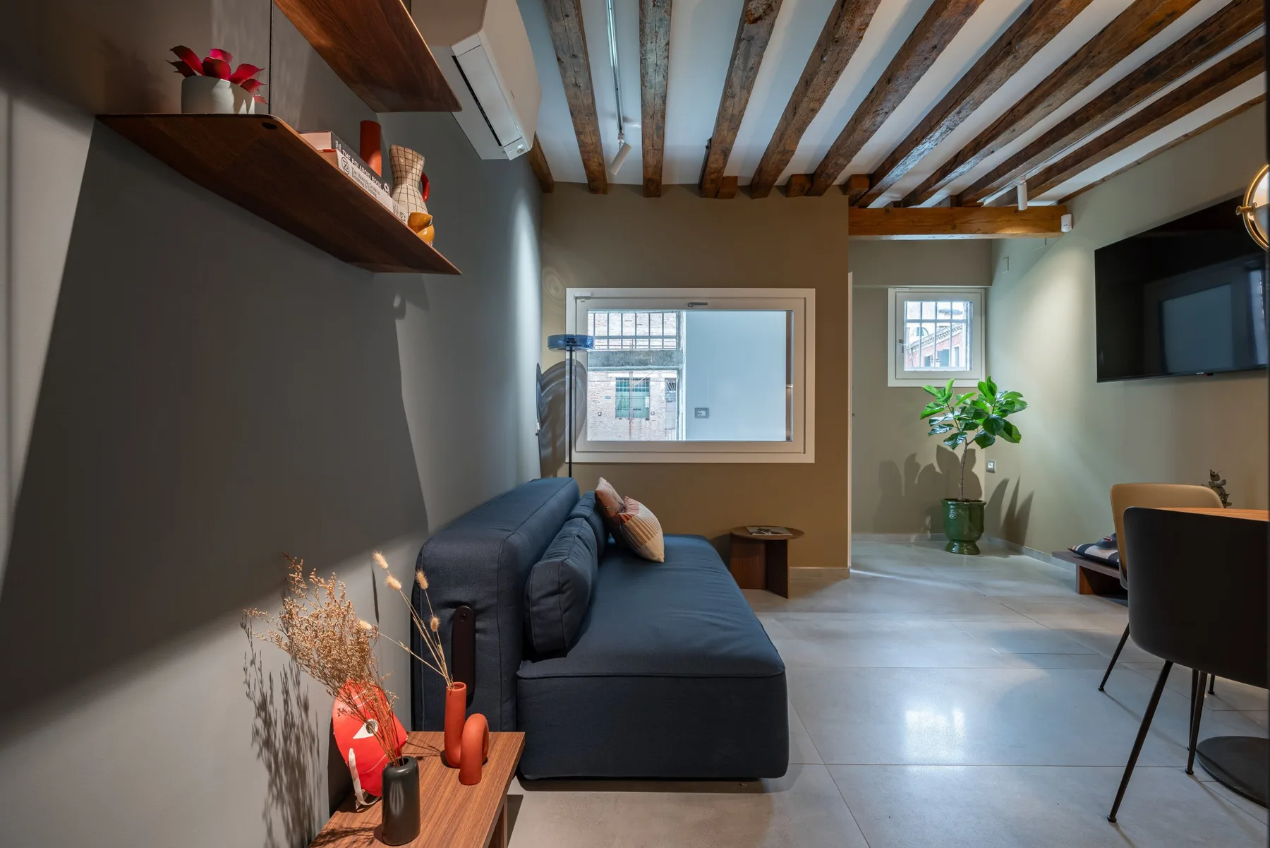 A living room with seating, a wall-mounted television, and exposed ceiling beams.