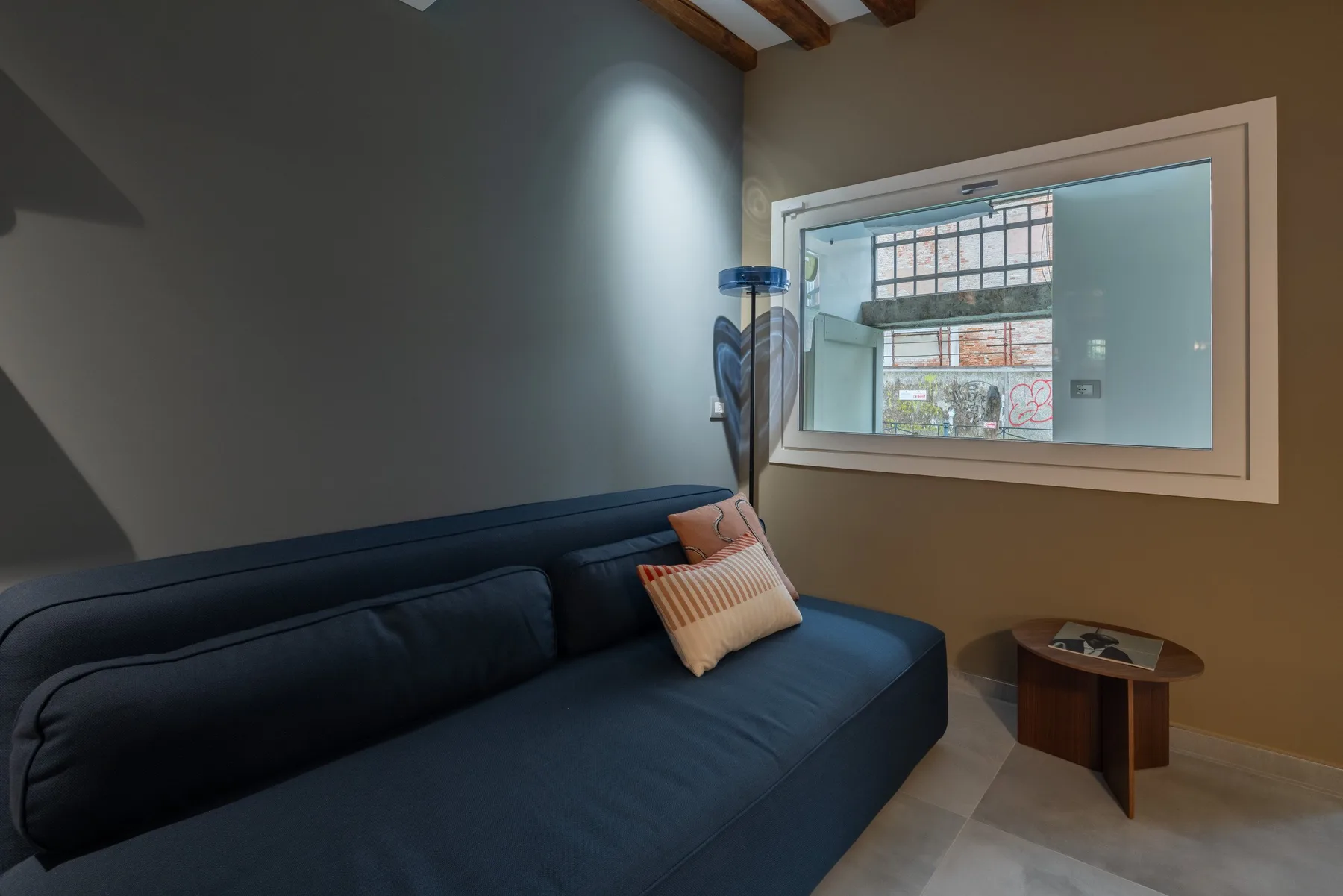 Una habitación con asientos oscuros, una mesa auxiliar pequeña y una ventana amplia.