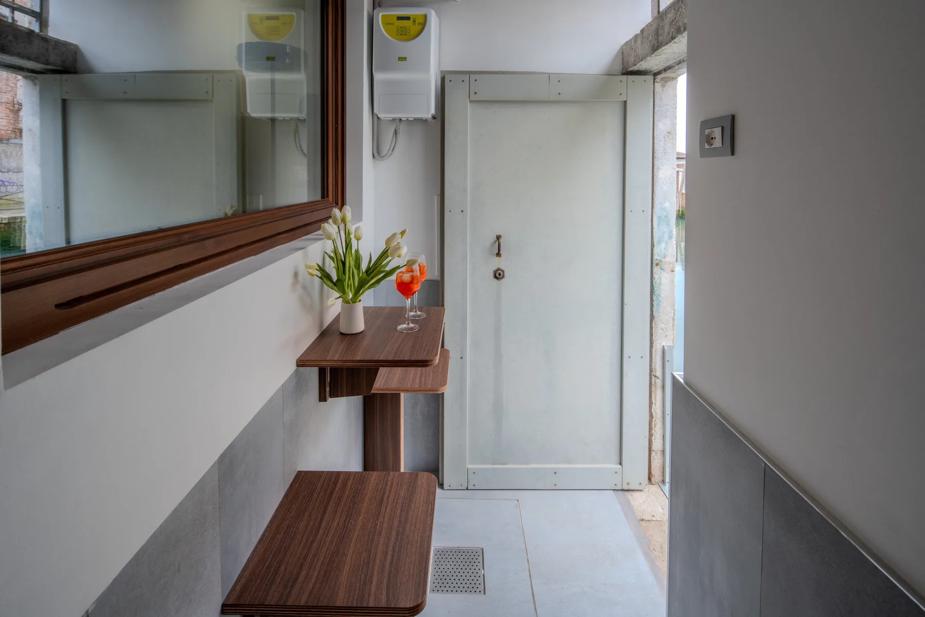 Un baño estrecho con ducha, espejo y pequeñas superficies de madera.