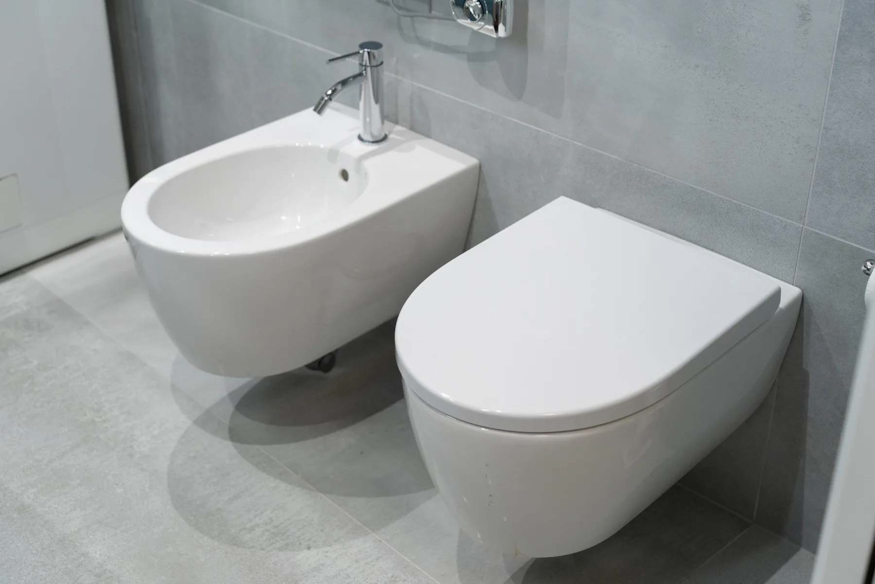 Un baño con un inodoro y un bidé junto a un grifo de pared.