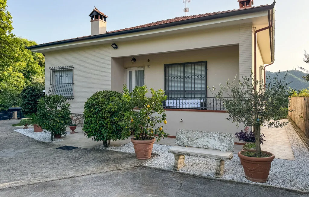 Exterior de una casa con porche cubierto, plantas en macetas y un banco de piedra.