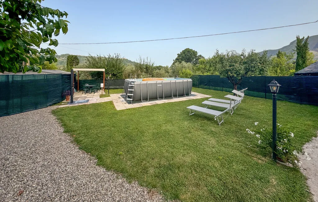 Un patio con césped tiene una piscina elevada y sillas reclinables.