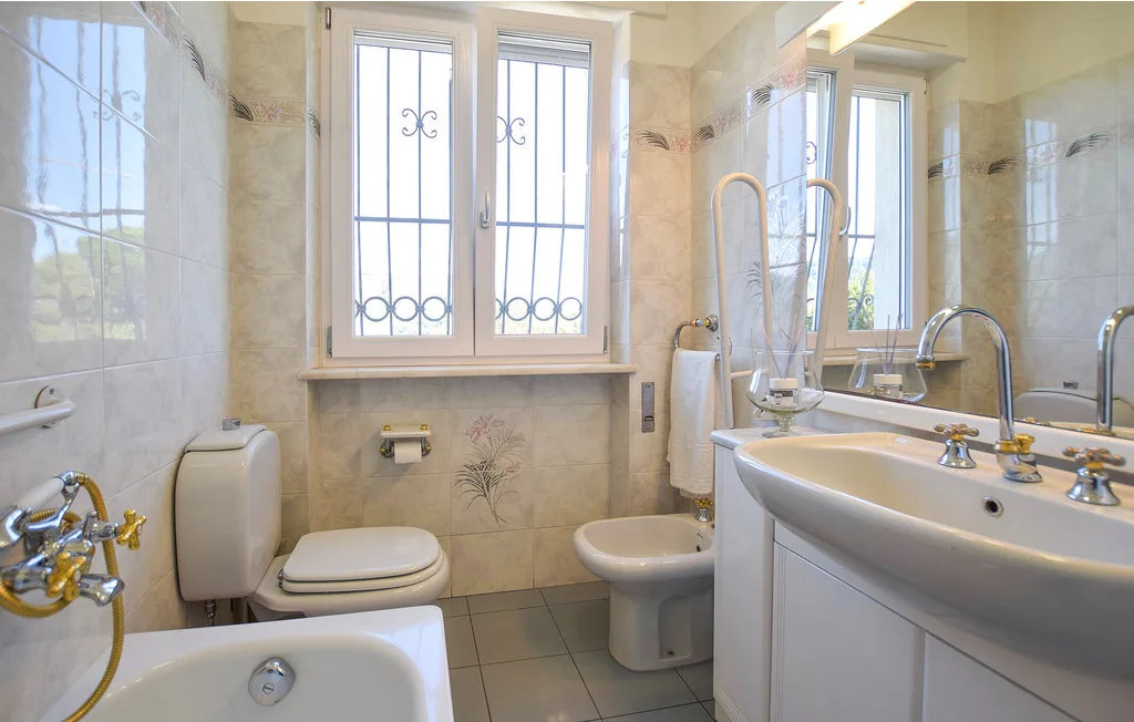 Un baño alicatado con bañera, inodoro, bidé y un lavabo ancho bajo las ventanas.