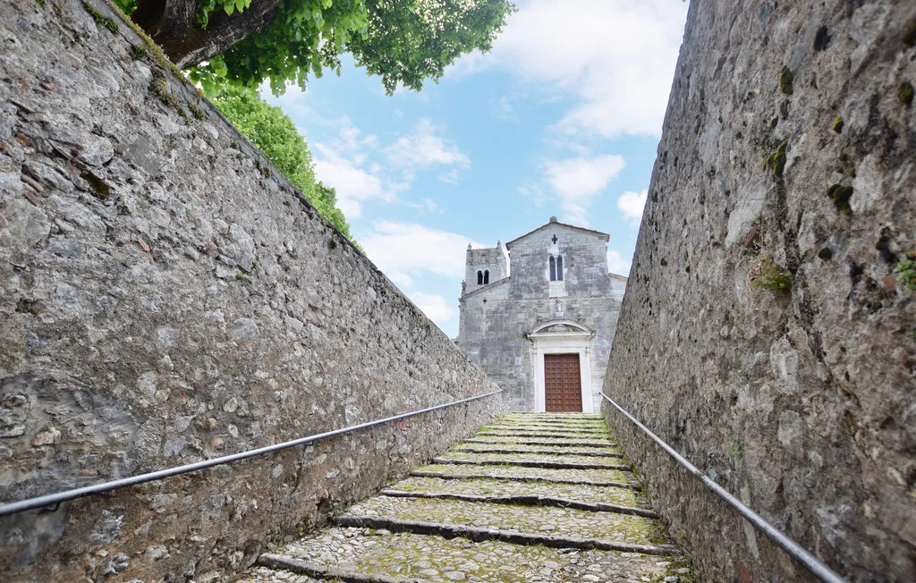 Una escalera de piedra asciende entre muros altos hacia una pequeña iglesia.