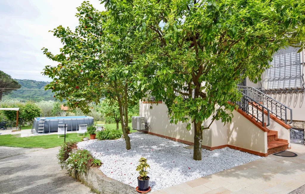 Una zona exterior ajardinada tiene árboles frondosos, un lecho de grava y escalones junto a un edificio.