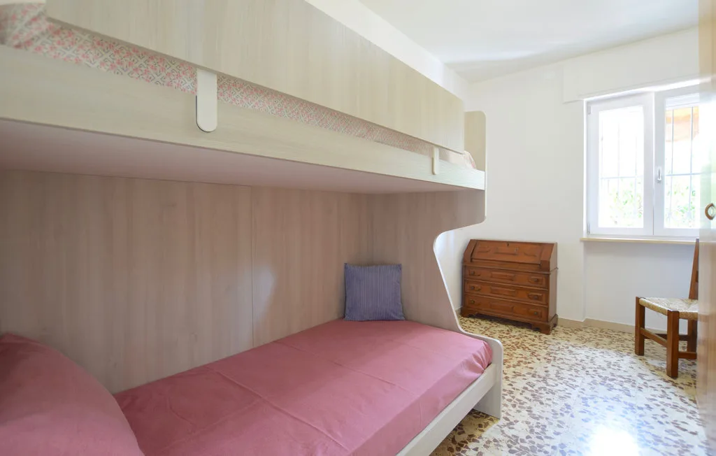 Un dormitorio con una cama rosa bajo una litera de madera y una ventana.