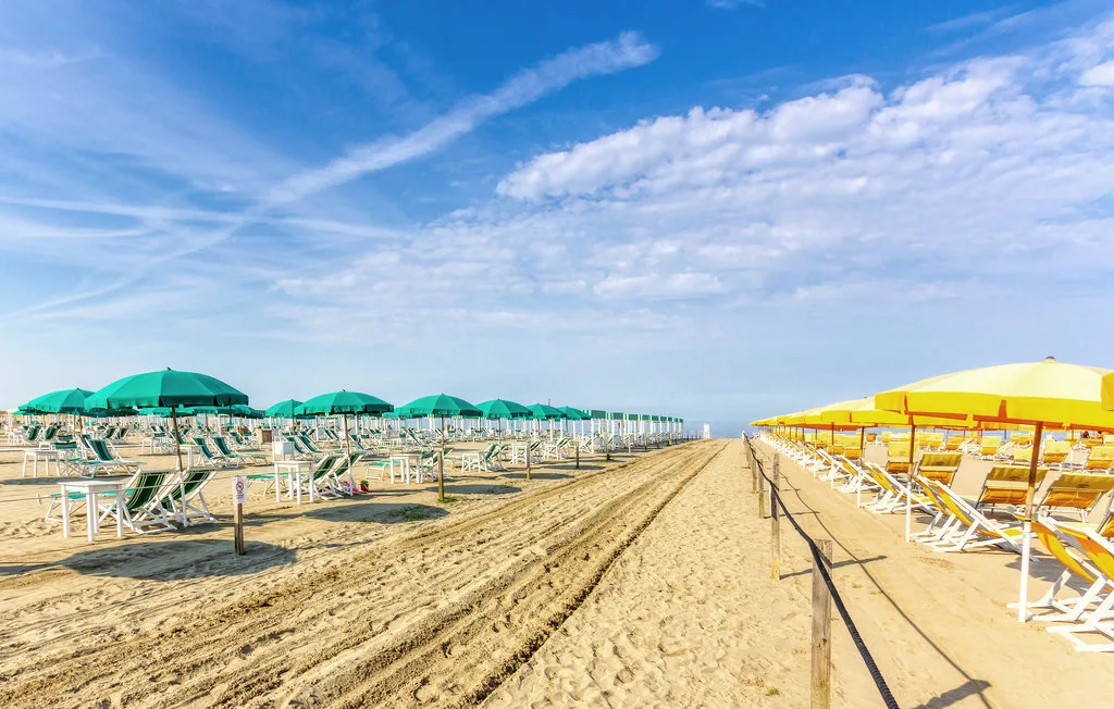 Un pasillo de arena atraviesa la playa entre filas de sombrillas de colores y tumbonas.