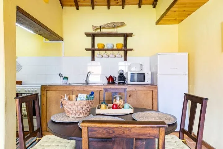 Una zona de comedor en la cocina con mesa de madera, sillas y electrodomésticos.