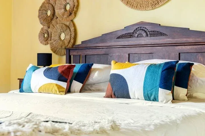 Un dormitorio con una cama tendida y almohadas coloridas junto a un cabecero de madera.