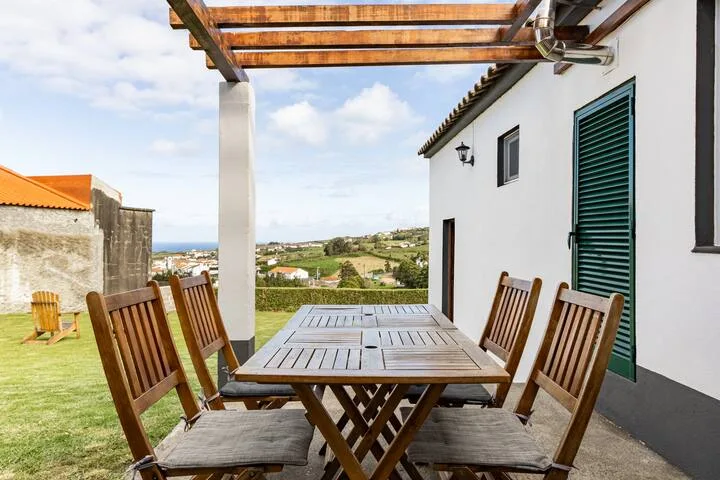 Un comedor en el patio con asientos de madera da a un jardín con césped y colinas.