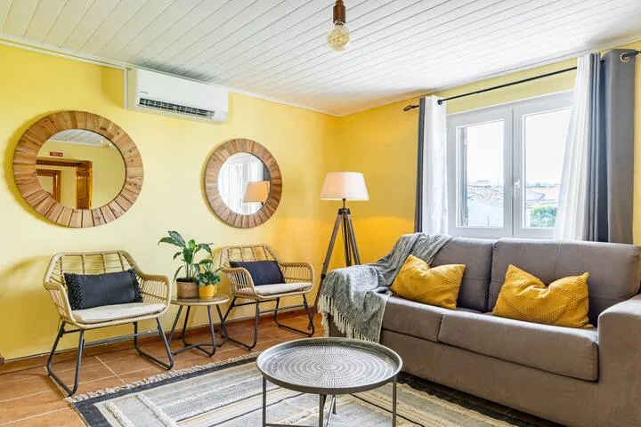 Una sala luminosa con asientos grises, sillas tejidas y paredes amarillas.