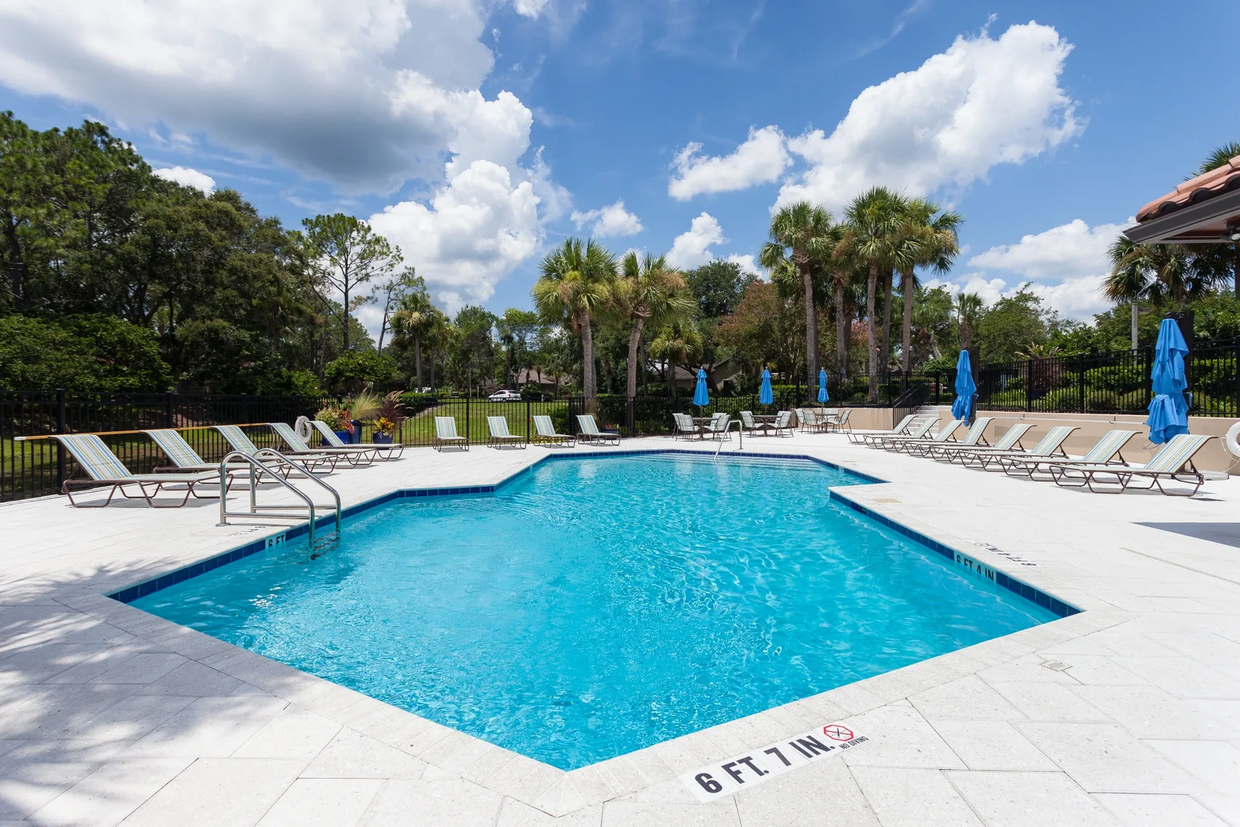 An outdoor swimming pool is surrounded by lounge seating and trees.