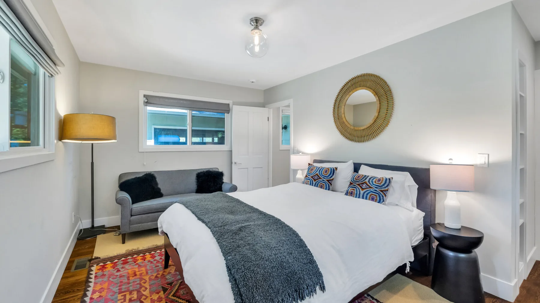 A bedroom with a large bed, gray seating, and colorful patterned rugs.