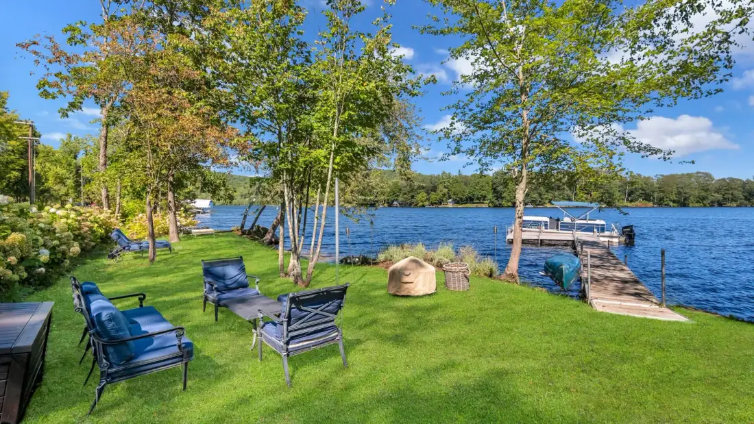 A grassy lakeside yard with outdoor seating and a wooden dock.