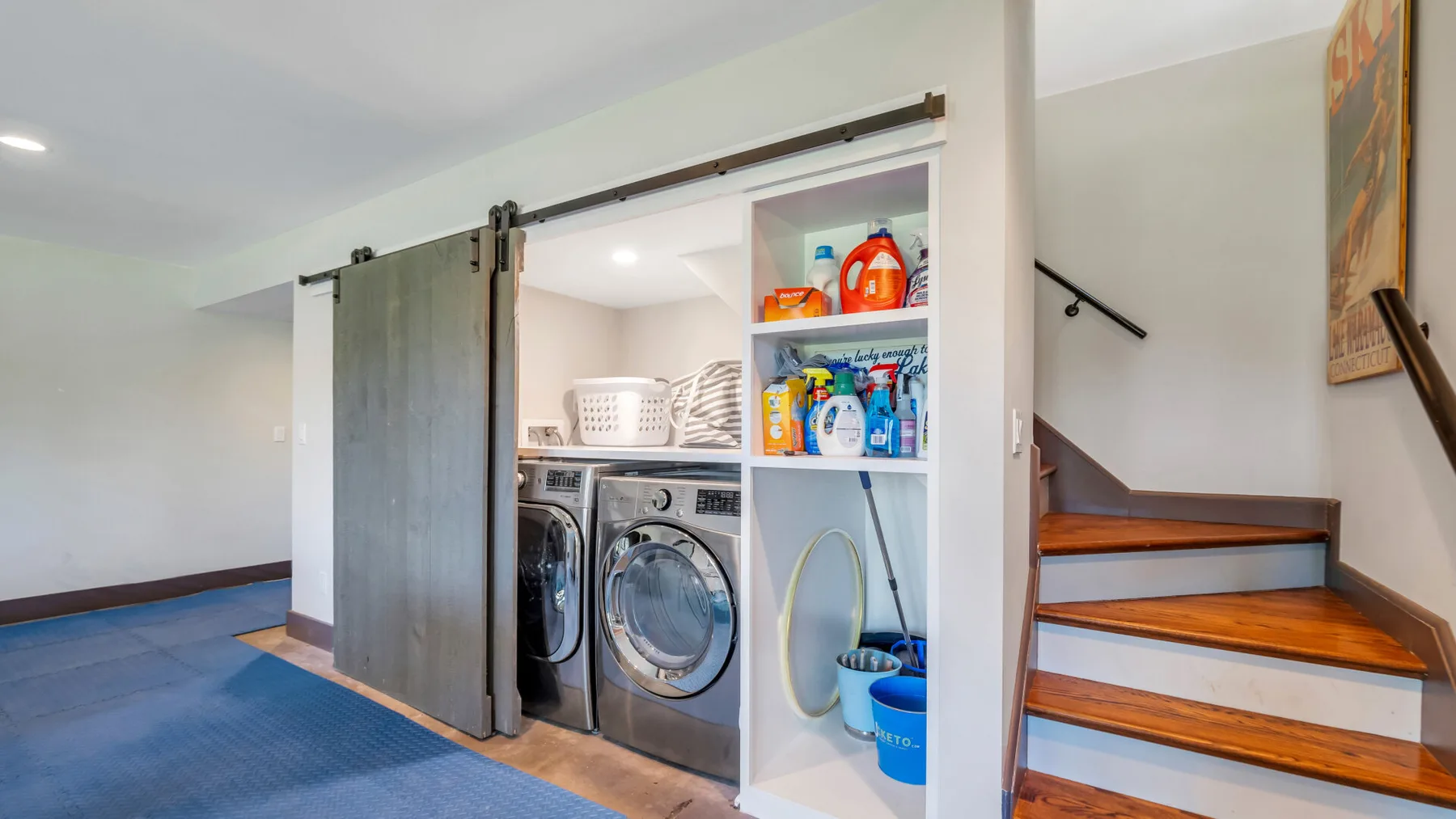 Laundry area with front-loading machines, open shelves, and stairs.