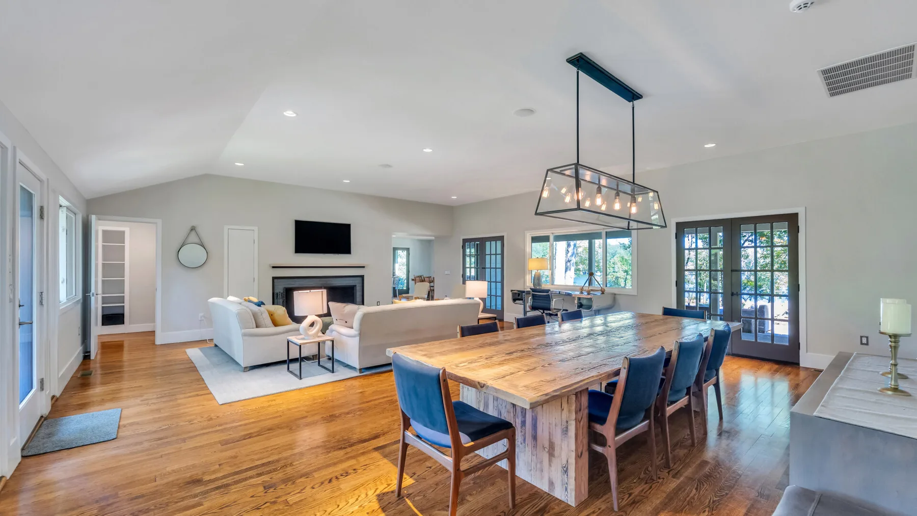 A bright open-plan dining and living area with a long wooden table and seating.
