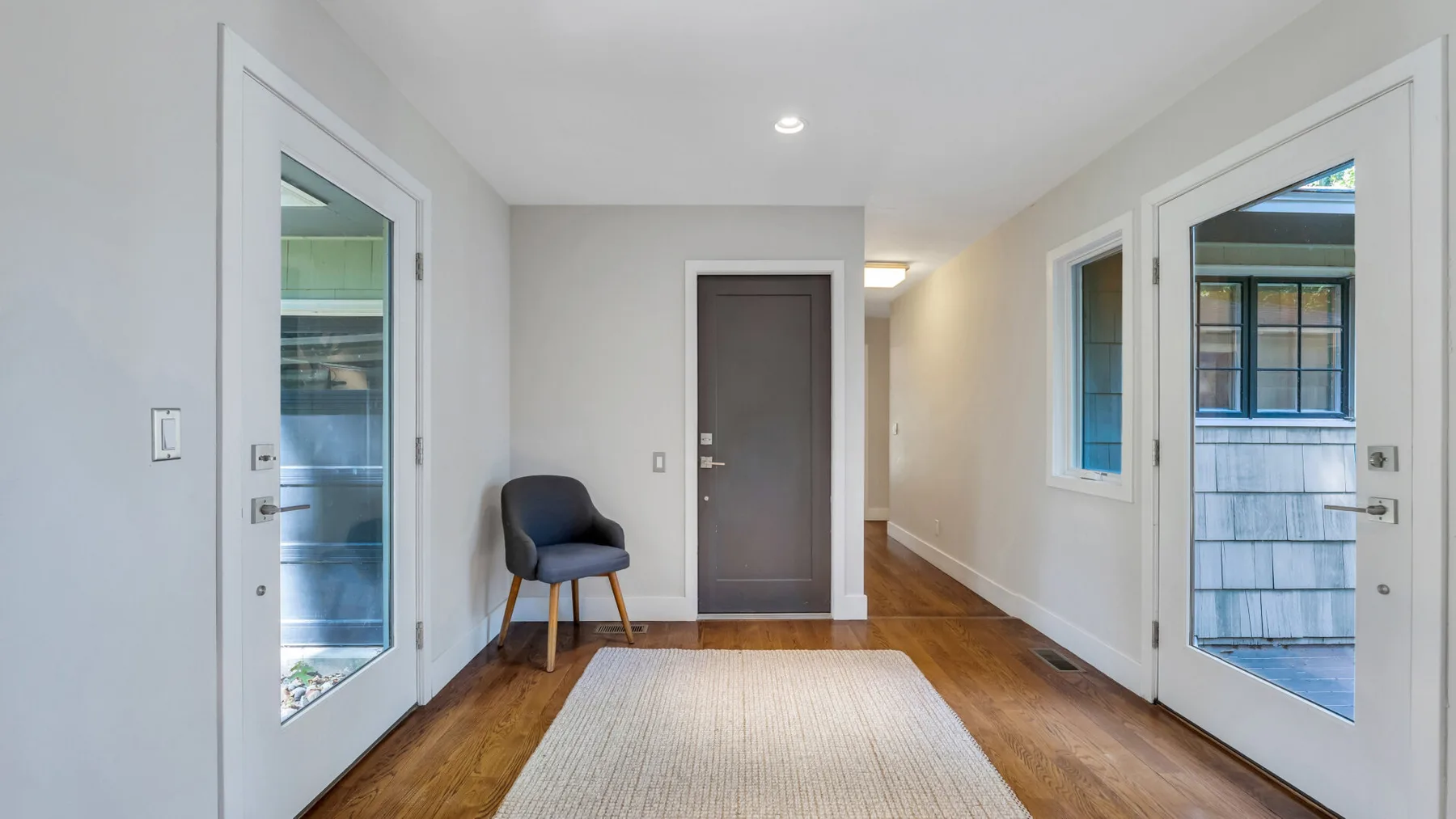 A bright entryway with a central door, wood flooring, and glass-paneled side doors.