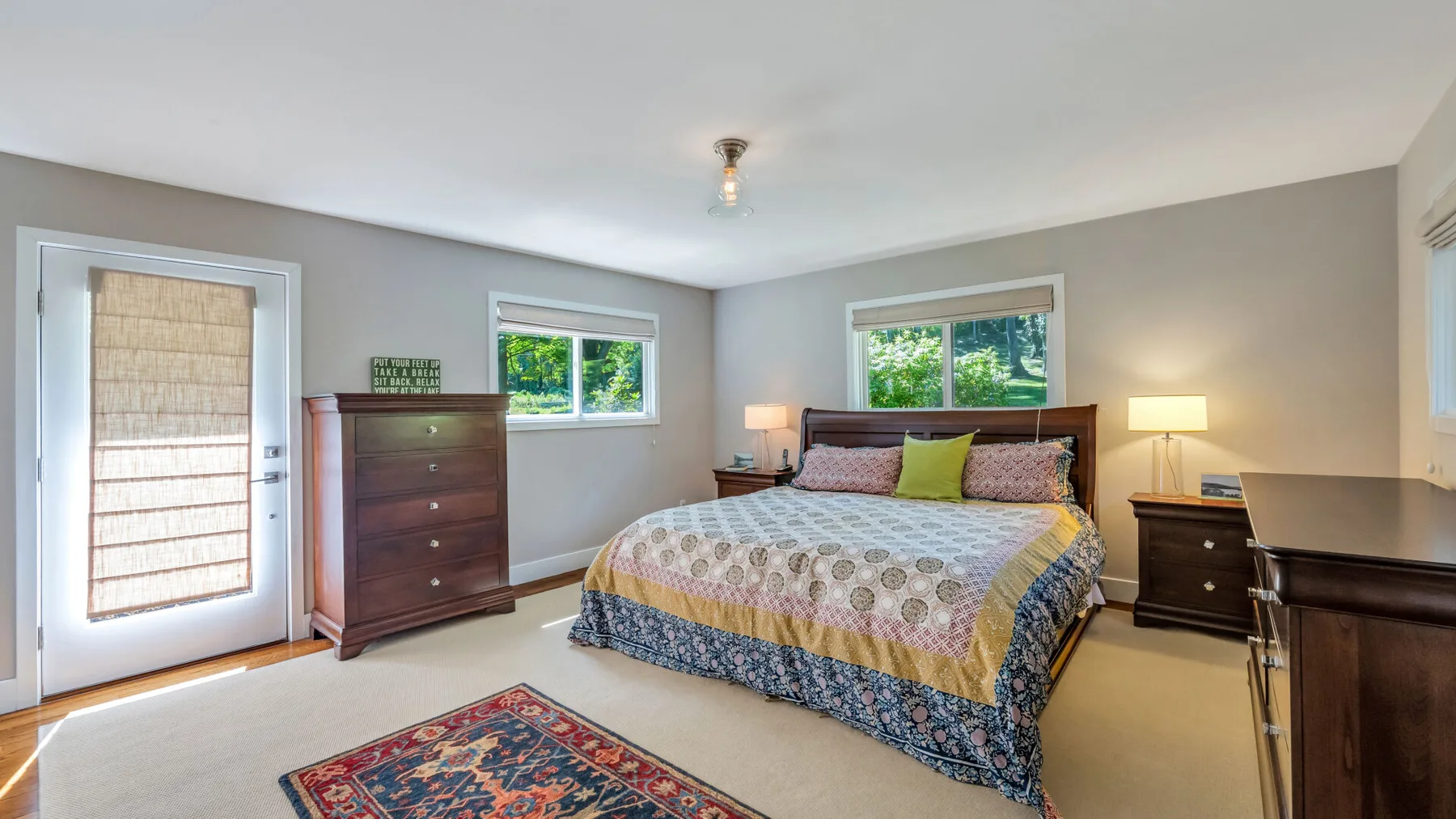 A bedroom with a bed, bedside tables, and windows overlooking greenery.