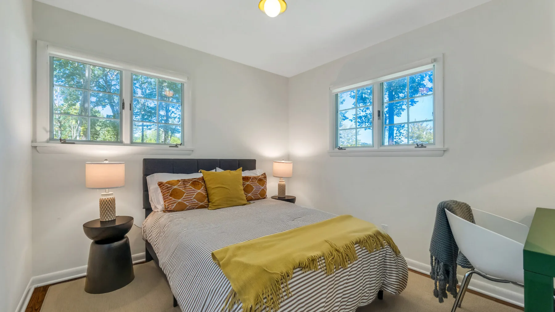 A bright bedroom with a bed beneath two windows and matching bedside lamps.