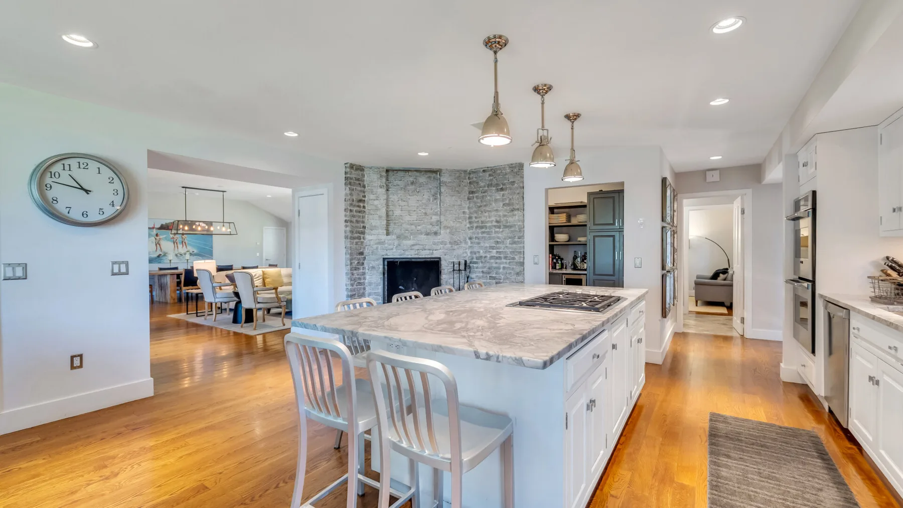 A bright kitchen with a central island and a stone fireplace beyond.