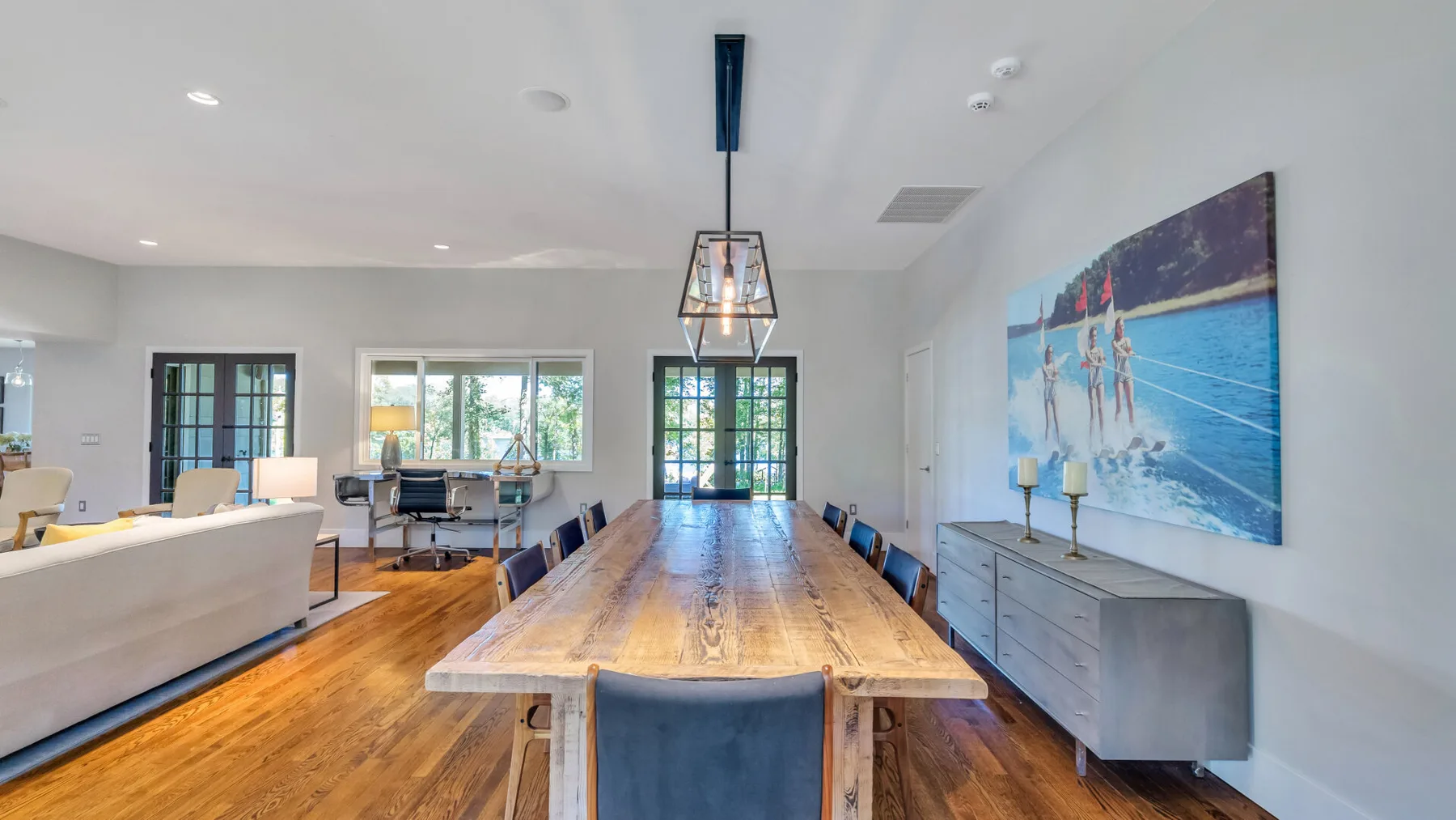 A dining area with a long wooden table, chairs, and large beach artwork.