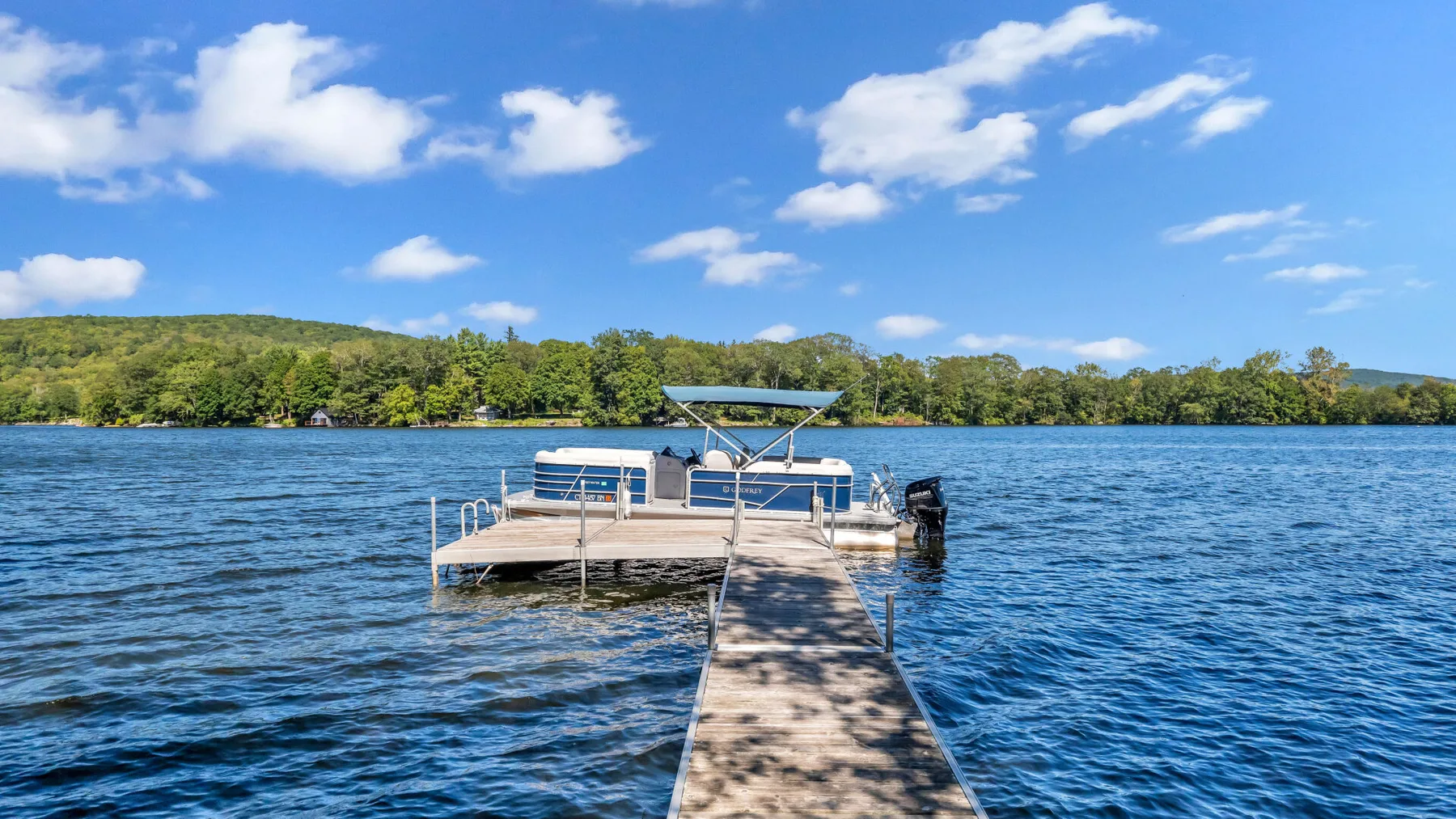 A wooden dock extends across a blue lake toward a small boat.