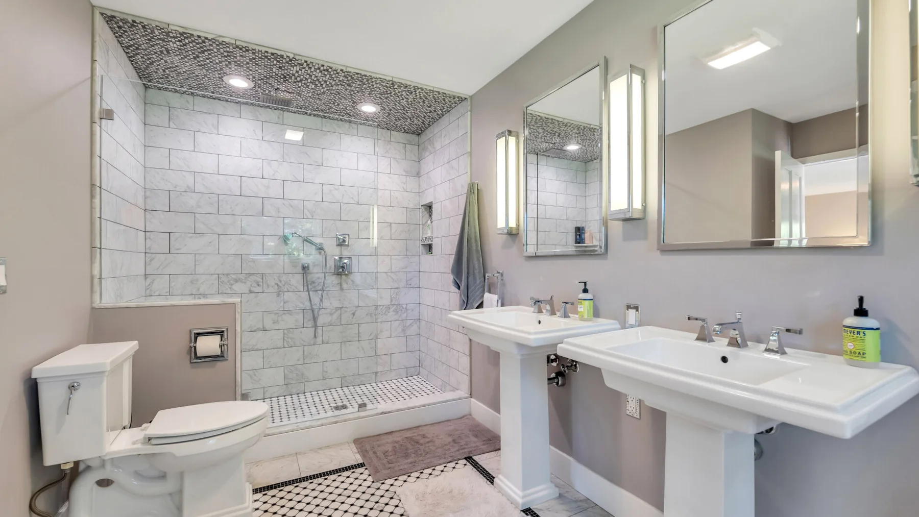 A bathroom with a tiled shower, a toilet, and a double sink.