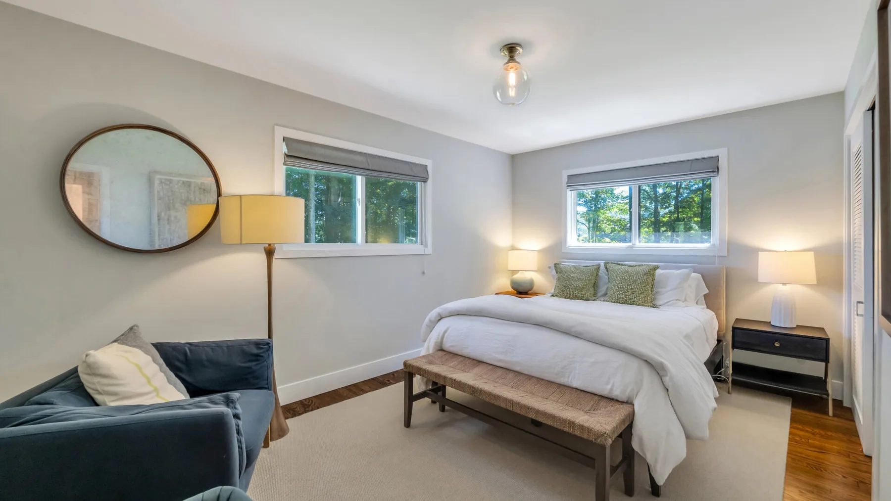 A bedroom with a bed, windows, and a seating area.