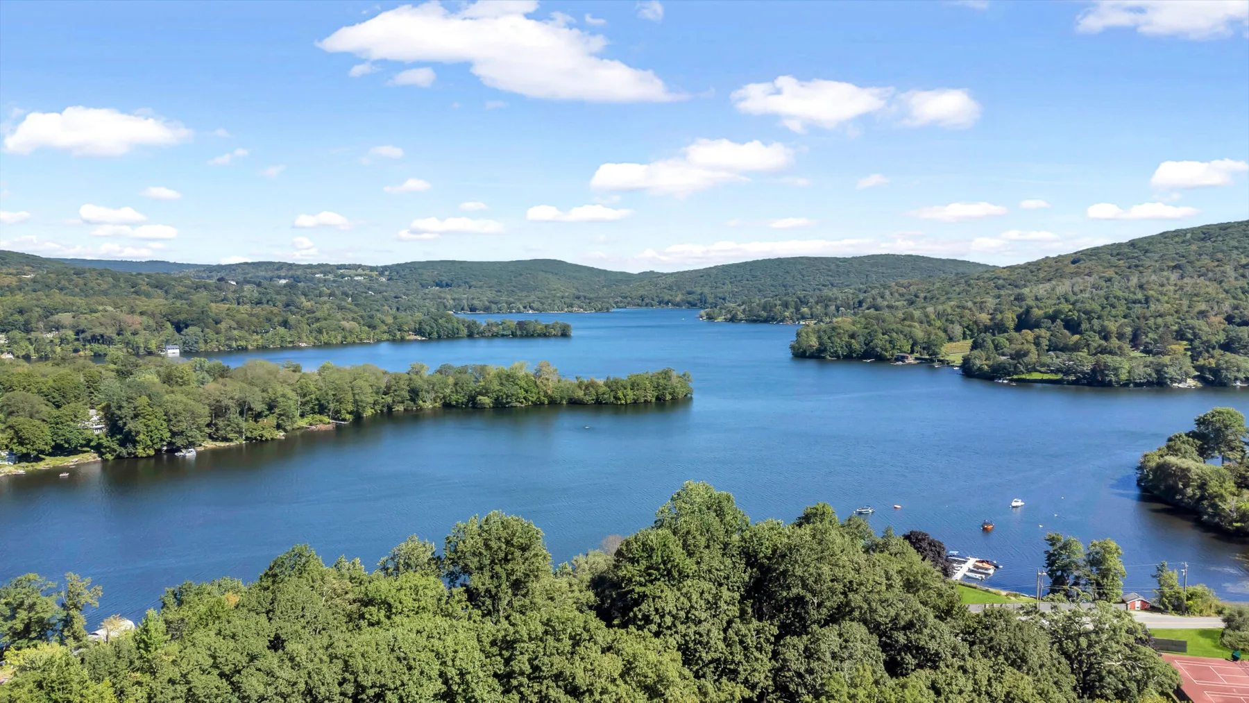 A broad lake winds through wooded hills beneath a partly cloudy sky.