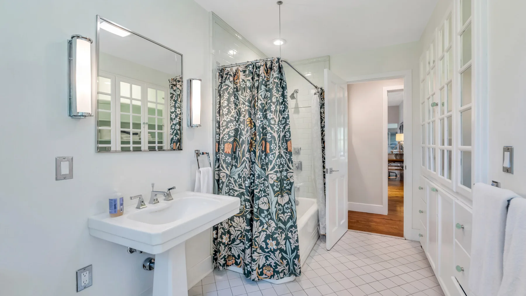 A bright bathroom with a sink, patterned shower curtain, and tiled floor.