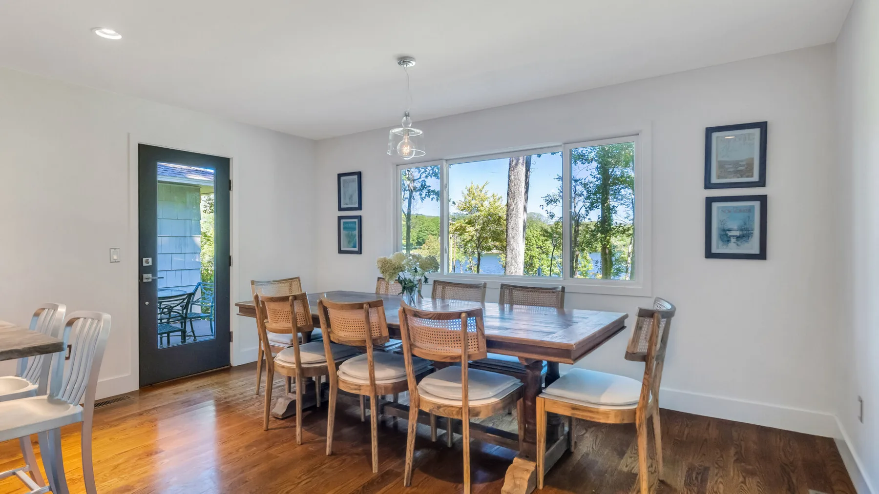 A dining room with a large wooden table and chairs beside broad windows.