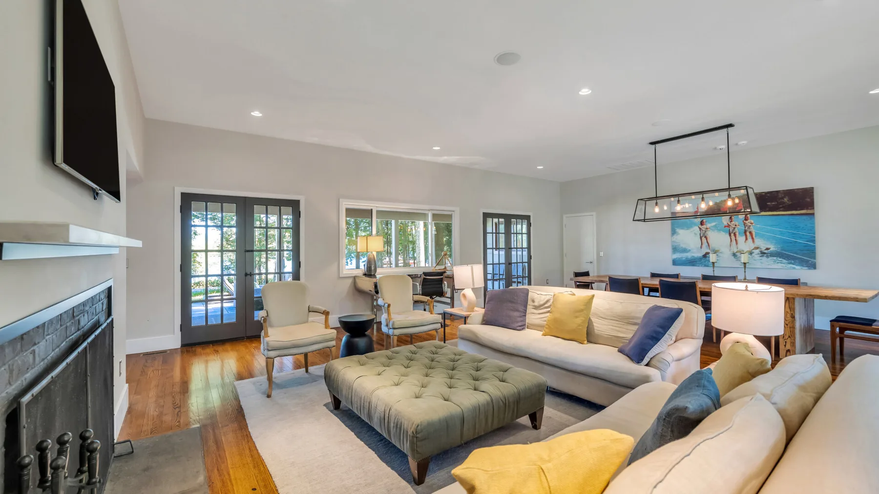 A bright living room with seating, a large ottoman, and windows opening onto a patio.