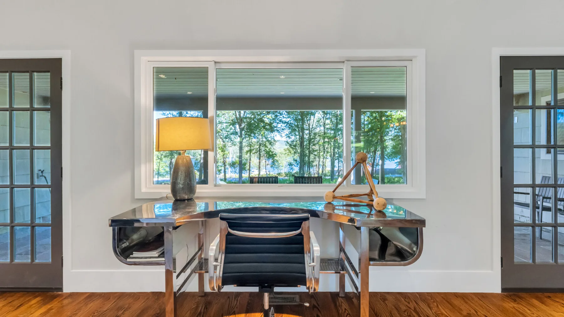 A bright home office with a desk, chair, and large window overlooking trees.