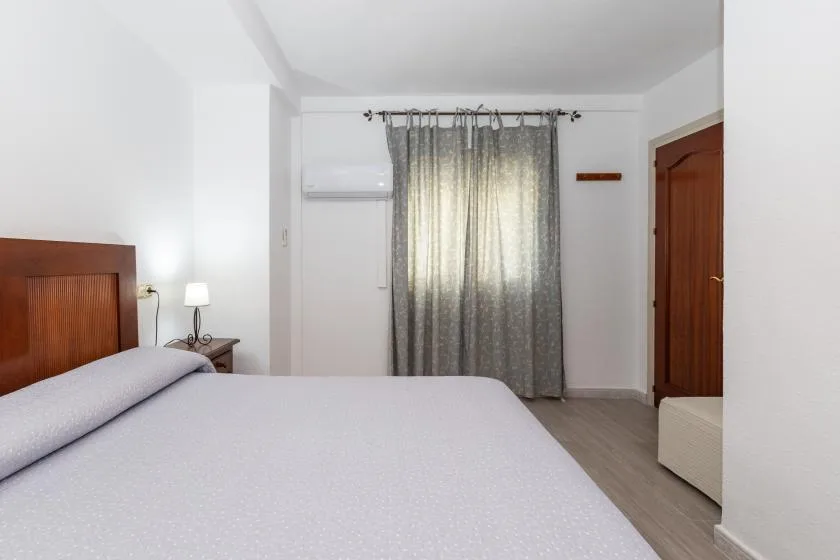A bedroom with a bed, gray curtains, and a wooden door.