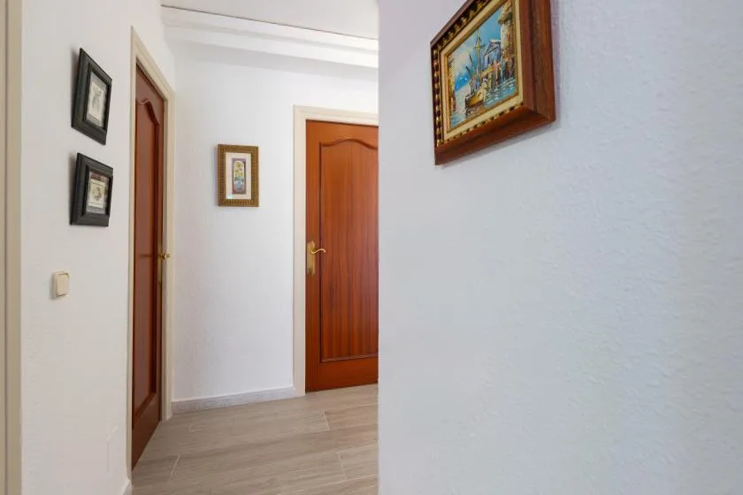 A white hallway with wooden doors and framed pictures on the walls.