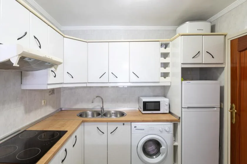 A compact kitchen with white cabinets, a cooktop, and a washing machine.