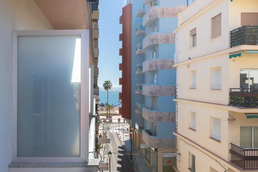 A narrow street runs between apartment buildings, with the sea visible in the distance.